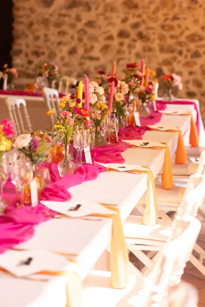 Table de mariage colorée dans des tons rose, orange, jaune, bouquet de fleurs et bougies